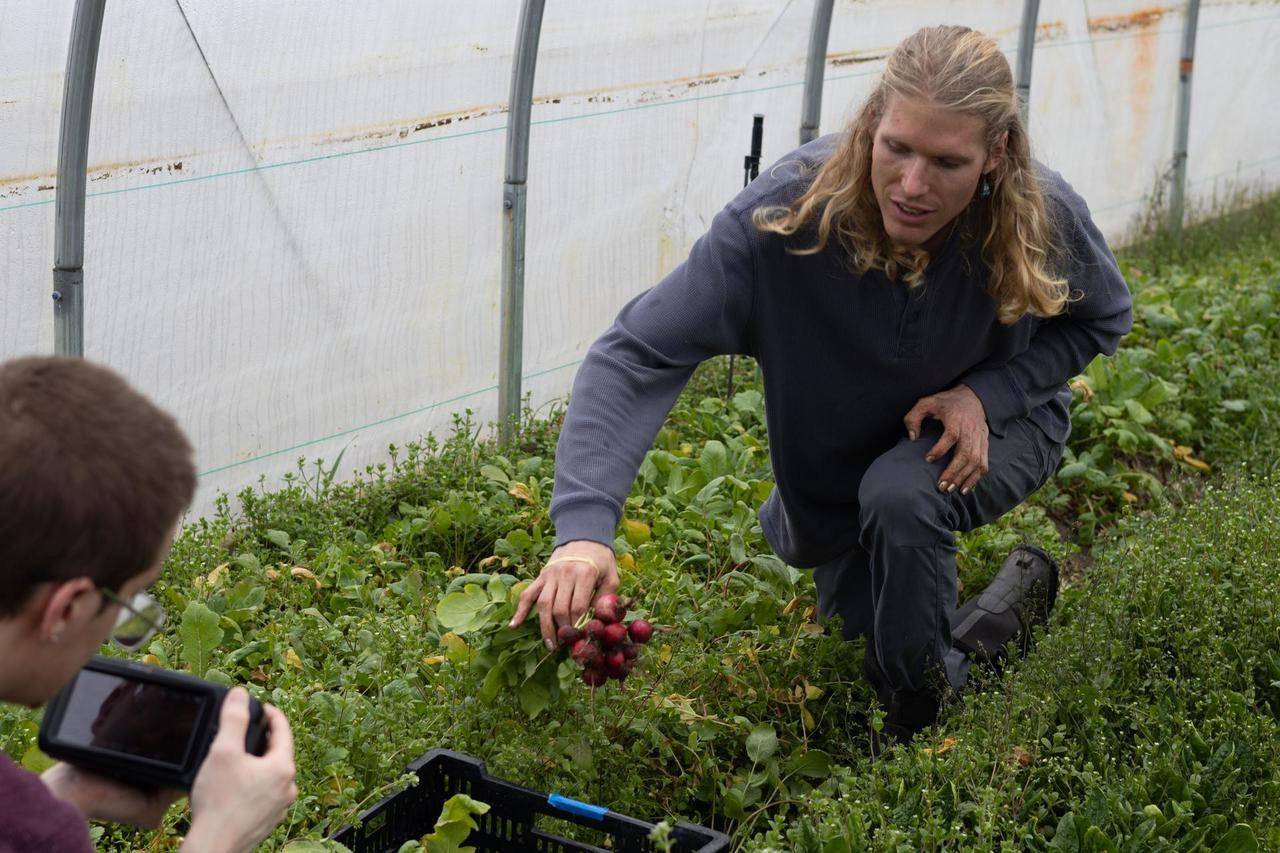 a student filming Isak Davis talking as he holds up a handful of radishes